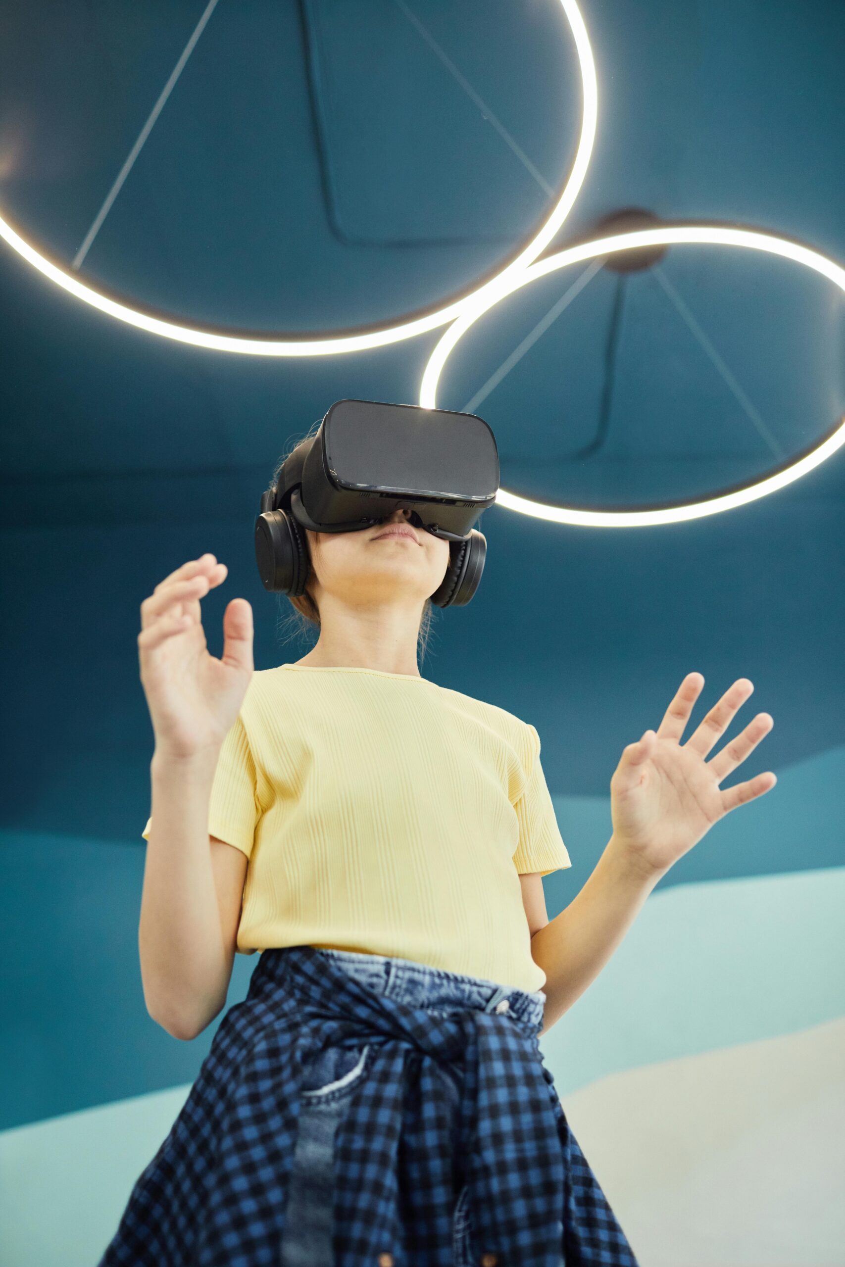 From below of anonymous girl standing with hands raised while experiencing virtual reality in studio